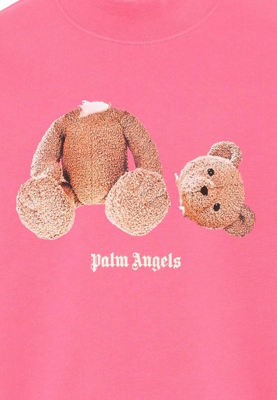 Ours en peluche démonté avec la tête détachée sur fond rose au-dessus du texte « Palm Angels » en police Old English blanche.