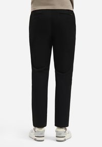 Zwarte broeken met een rechte pasvorm, voorzien van twee achterzakken, subtiele stiksels en gedragen met witte sneakers.