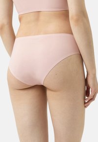 Slip in cotone rosa chiaro con design senza cuciture, copertura moderata e texture liscia. Presenta un logo discreto sulla fascia elastica.