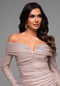 Off-shoulder mauve klänning med strukturerad, plisserad tyg och en djup V-ringning. Silverfärgade blommörhängen kompletterar stilen.