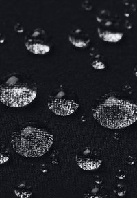 Gotas de agua sobre una superficie de tela negra texturada, mostrando diversos tamaños y cualidades reflectantes de las gotas contra el fondo oscuro.