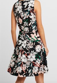 Černé květinové šaty s přiléhavým korzetem, rozšířenou sukní a bezrukávovým designem. Obsahují bílé a růžové květiny s zelenými akcenty.