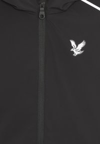 Schwarze Kapuzenjacke mit Frontreißverschluss, versehen mit einem weißen Adler-Logo und kontrastierenden weißen Akzenten auf den Schultern. Glattes, leichtes Gewebe.