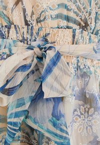 Robe légère en tissu imprimé avec des rayures bleues et une broderie florale. Elle présente une taille froncée et une ceinture nouée en détail.