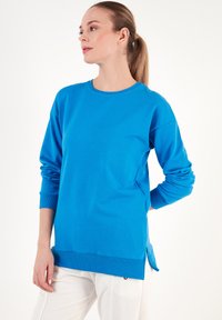 Sudadera azul con mangas largas, cuello redondo, puños y dobladillo acanalados, aberturas laterales en la parte inferior, hecha de suave material de algodón.