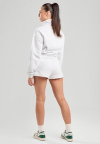 Light gray cropped sweatshirt with high collar and matching shorts, made of soft fabric. Model wears white socks and green-accented sneakers.