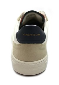 Sneaker bianca con pannello posteriore in suede beige, dettagli in pelle blu navy e branding dorato "AMBITIOUS" sul colletto posteriore e suola testurizzata.