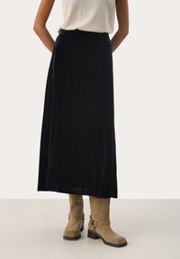 Gonna maxi in velluto blu navy con una trama liscia e una leggera lucentezza, abbinata a stivali in suede beige con dettagli in fibbia.