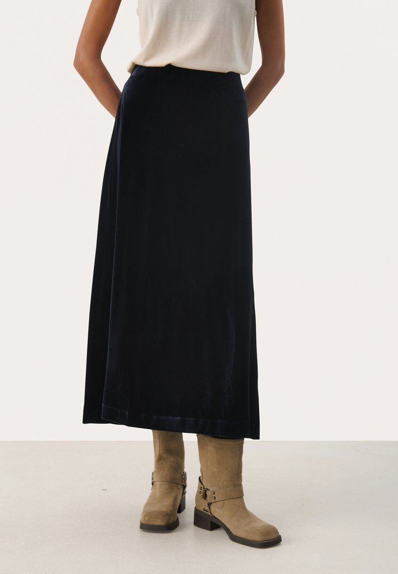 Gonna maxi in velluto blu navy con una trama liscia e una leggera lucentezza, abbinata a stivali in suede beige con dettagli in fibbia.