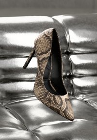 Chaussure à talon haut à bout pointu avec un imprimé serpent beige et marron, une silhouette élégante et une doublure intérieure noire.