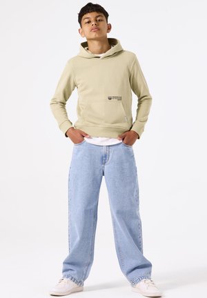 Lichtgroene hoodie met een voorzak en geprinte tekst, gecombineerd met lichtblauwe baggy jeans. Minimalistische witte sneakers maken de look compleet.