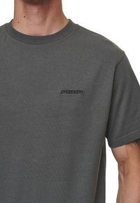 Grå bomulls t-skjorte med rund hals og korte ermer. Har en brodert logo i mørkere grå på brystet. Glatt tekstur.