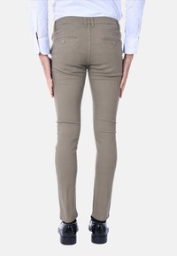 Pantaloni khaki slim-fit con tessuto texturizzato, due tasche posteriori e design a gamba dritta, abbinati a scarpe nere.
