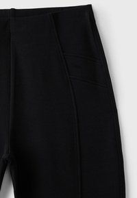 Pantalon noir avec taille élastique et détail de poche visible sur la couture latérale sur un fond clair uni.