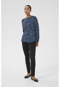 Mörkblå mönstrad blus med långa ärmar och rund halsringning, bärs tillsammans med svarta slim-fit byxor och svarta ballerina. Enkel bakgrund.