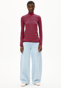 Rot-blau gestreiftes Langarm-Turtleneck-Oberteil, kombiniert mit hellblauen Schlagjeans und cremefarbenen Schuhen.