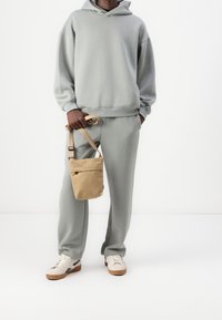 Lysegrå hættetrøje og joggingbukser med en afslappet pasform, kombineret med en beige crossbody taske og cremefarvede sneakers med brune detaljer.