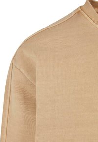 Suéter beige de cuello redondo con tejido acanalado texturizado, que presenta un acabado suave y un diseño de hombros sin costuras, enfatizando un estilo minimalista.