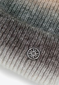 Cappello in maglia con tonalità grigie sfumate e motivo testurizzato. Presenta un dettaglio in metallo argento con il logo. Tessuto morbido e caldo.