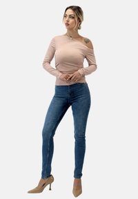 Ljusrosa av-shoulder långärmad topp som matchas med tajta blå jeans och nude högklackade skor. Toppen har en slät textur och en figurnära design.