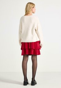 Maglione bianco e soffice in maglia abbinato a una mini gonna a strati in velluto rosso. La modella indossa collant neri e scarpe nere chunky.