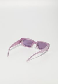 Lunettes de soleil translucides violettes avec des verres rectangulaires, des branches fines et un design géométrique. Présente un détail de charnière discret.