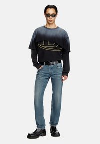 Black and faded gray layered graphic long-sleeve shirt, blue denim jeans, black chunky boots, black rectangular sunglasses.