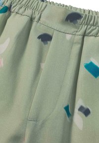 Groene stof met abstracte patronen in teal, marineblauw en roze. Kenmerkt zich door een elastische tailleband en een zijzak. Gladde textuur.