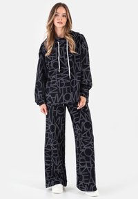 Czarna bluza z kapturem i pasujące szerokie spodnie z wyróżniającym się szarym wzorem tekstowym. Z przodu duża kieszeń typu kangur oraz regulowane sznurki.