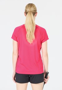 Lyhythihainen urheilupaita, joka on tiukasti istuva kirkkaan pinkkinä, yhdistettynä mustiin shortseihin. Siinä on sileä, kosteutta siirtävä kangas ja rento istuvuus.