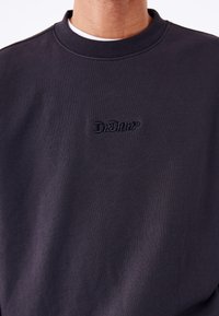 Sudadera de algodón gris oscuro con cuello redondo y logo bordado "Dr. Denim" en el pecho. Textura suave, diseño minimalista.
