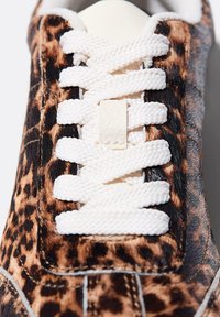 Baskets à imprimé léopard avec une tige en fourrure texturée marron et noire, des lacets blancs et une languette lisse beige. Détails cousus le long des côtés.