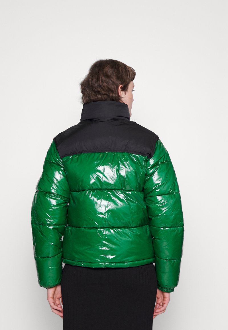 Pufferjack met een glanzend groene romp en een zwart schoudergedeelte. Voorzien van een hoge kraag en een horizontaal doorgestikt patroon. Gemaakt van een glanzend materiaal.