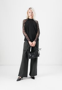 Black top with lace long sleeves, loose fit; gray wide-leg trousers; black textured handbag. High-heeled black shoes with pointed toes.