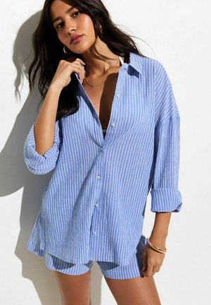 Chemise à rayures bleues et blanches à boutons, manches retroussées, associée à un short assorti. Tissu léger avec une coupe décontractée.