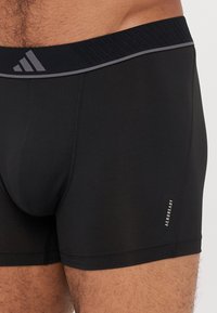 Schwarze sportliche Boxershorts mit geripptem Bund und reflektierendem Logo. Glattes Material mit flachen Nähten, ausgestattet mit feuchtigkeitsableitender Technologie.