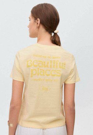 T-shirt jaune à manches courtes avec une coupe décontractée. Le dos présente un texte jaune clair indiquant "Il y a tant de beaux endroits que je n'ai pas encore vus."