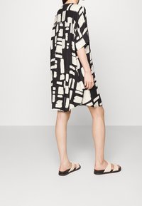 Svart och krämfärgad knä-lång klänning med en boxig design, som har abstrakta penseldrag-mönster, korta ärmar och en avslappnad passform. Bärs med sandaler.