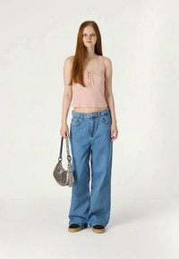 Top cropped cor-de-rosa com laço decorativo, combinado com jeans de perna larga azul claro. A modelo segura uma pequena bolsa prateada.