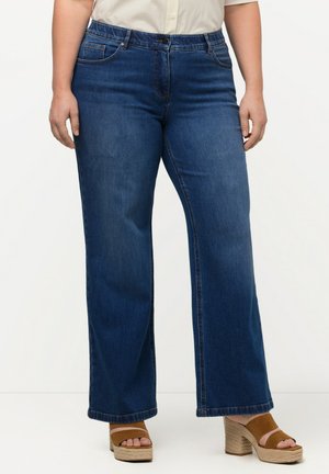 Jeans a gamba larga in denim scuro con vita alta, dotati di tasche frontali e delicate cuciture. Indossati con sandali con plateau marroni.