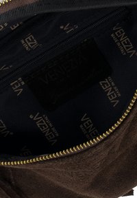 Innenraum einer braunen Wildledertasche mit schwarzer Stoffauskleidung, goldfarbenem "Venezia"-Logo, Reißverschluss und strukturierter Oberfläche.