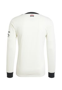 Maillot blanc à manches longues avec un tissu texturé. Poignets et col noirs, avec un petit logo sur la manche gauche et un détail au niveau de la nuque à l’arrière.