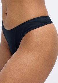 Svart bikiniunderdel i ett mjukt tyg, med låg midja och rena sömmar, som visar en minimalistisk och funktionell estetik.