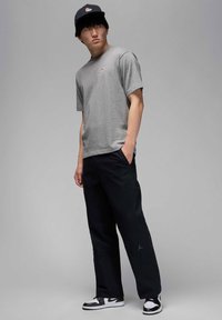 Gray crew-neck t-shirt, black loose-fit pants, black cap with logo, and black-and-white sneakers. Minimalistic design with logo accents.