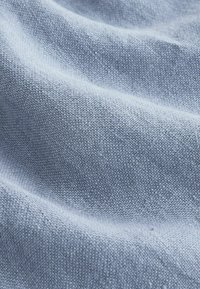 Tissu tissé bleu clair avec une surface texturée, légèrement surélevée et des plis doux créant des ombres douces.