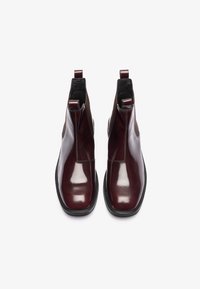 Bottines en cuir bourgogne avec une finition brillante, dotées de panneaux élastiques sur les côtés et de tirettes, montées sur une semelle noire plate.