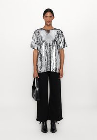 Silver sequins topp med korta ärmar, rund halsringning, i kombination med svarta vida byxor och svarta ankelskot. Håller en svart handväska.