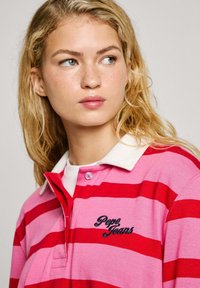 Raudonas ir rožinis dryžuotas polo marškinėliai su balta apykakle, su išsiuvinėtu "Pepe Jeans" logotipu ant kairiojo krūtinės, pagaminti iš minkštos medžiagos.