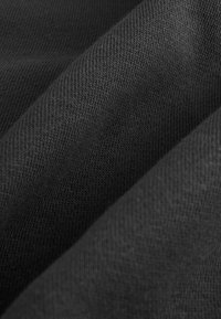 Tela de punto negra con una textura suave, que presenta una fina y uniforme canaladura. El material crea pliegues sutiles que enfatizan su flexibilidad.