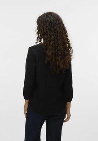Zwarte gebreide trui met driekwart mouwen, een gestructureerd patroon en een ronde zoom. Gekocht met donkere, losse jeans.